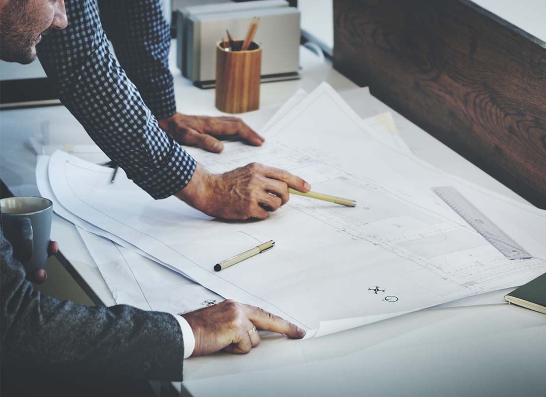 Architect Insurance - Close-up of Architect and Fellow Colleague Examining an Architectural Design Blueprint on a Desk during a Project Meeting Discussion